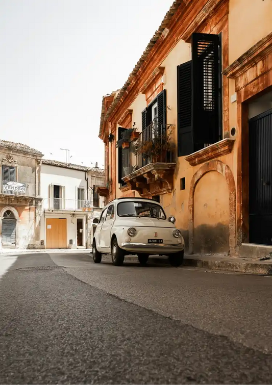 White vintage car canvas painting on a cobblestone street in an Italian village with terracotta facades